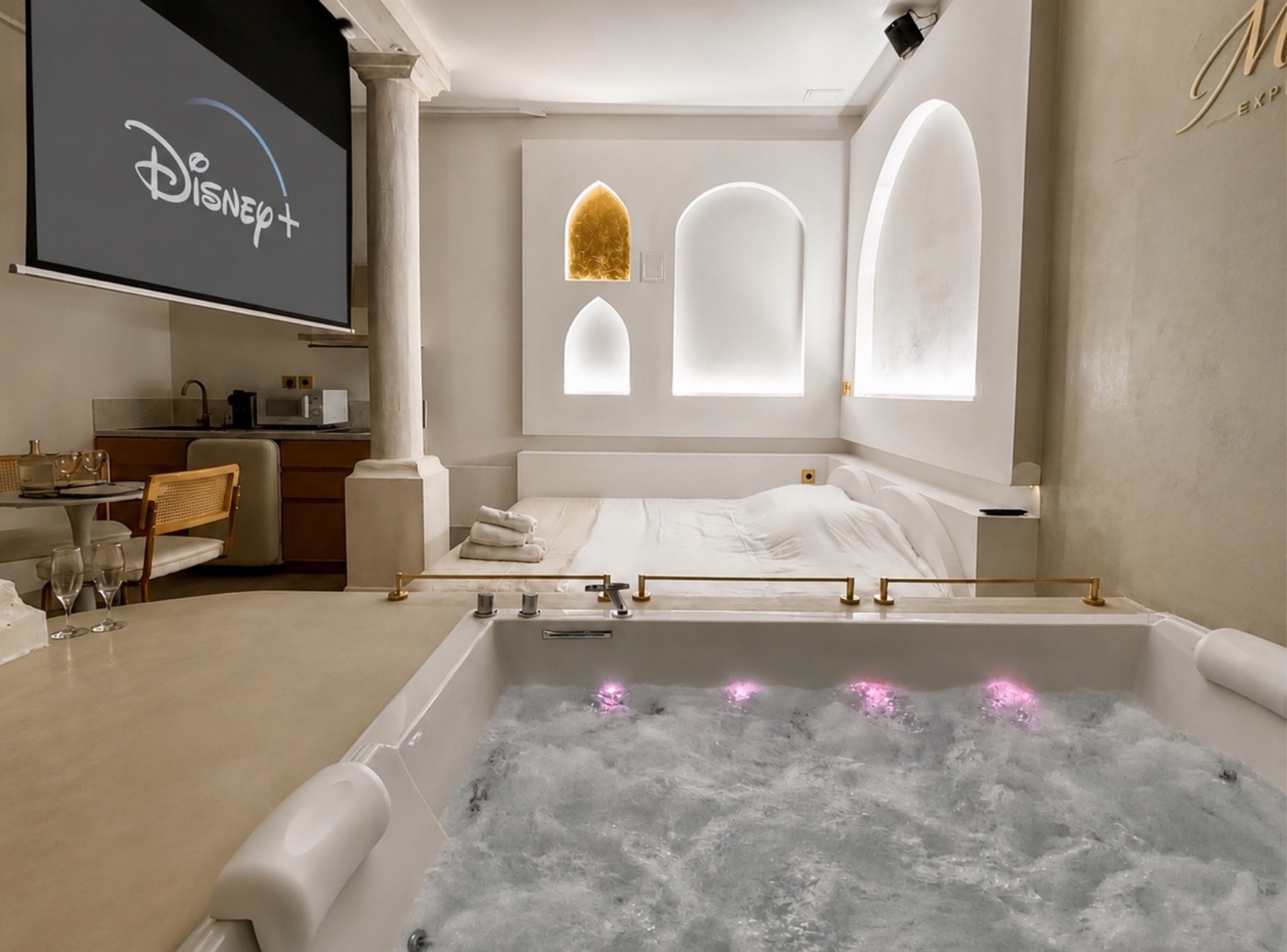 Suite Balnéo Room à Tarbes : jacuzzi privé, colonnade, arches blanches inspirées de Mykonos et grand écran
