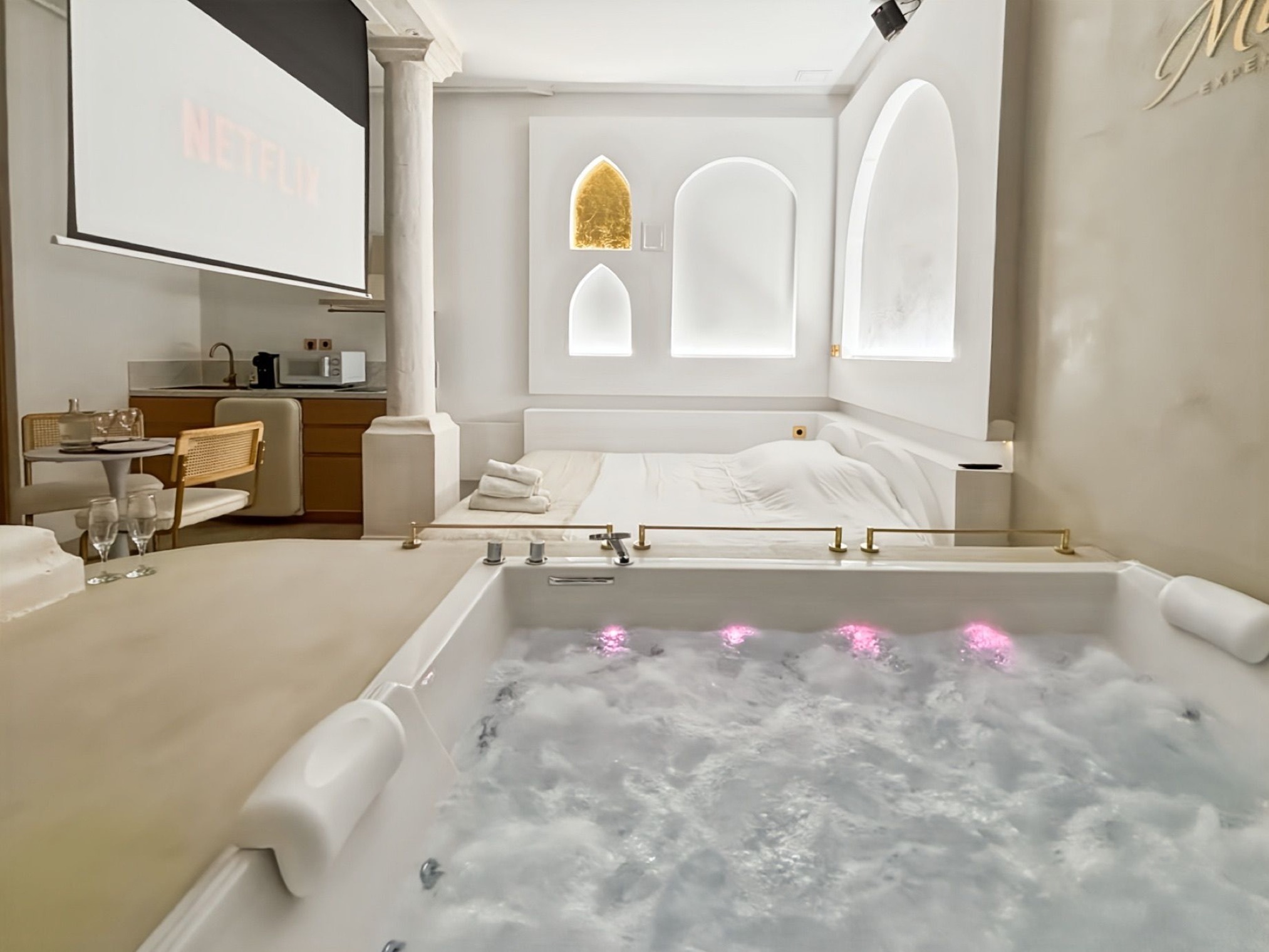 Vue large de la Balnéo Room avec jacuzzi illuminé, écran et coin repas